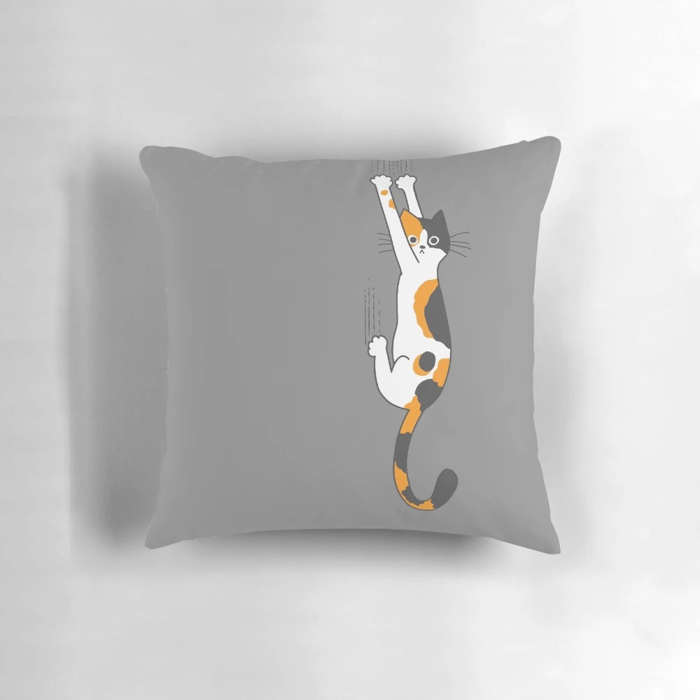Calico cat humorously clinging to a plush throw pillow