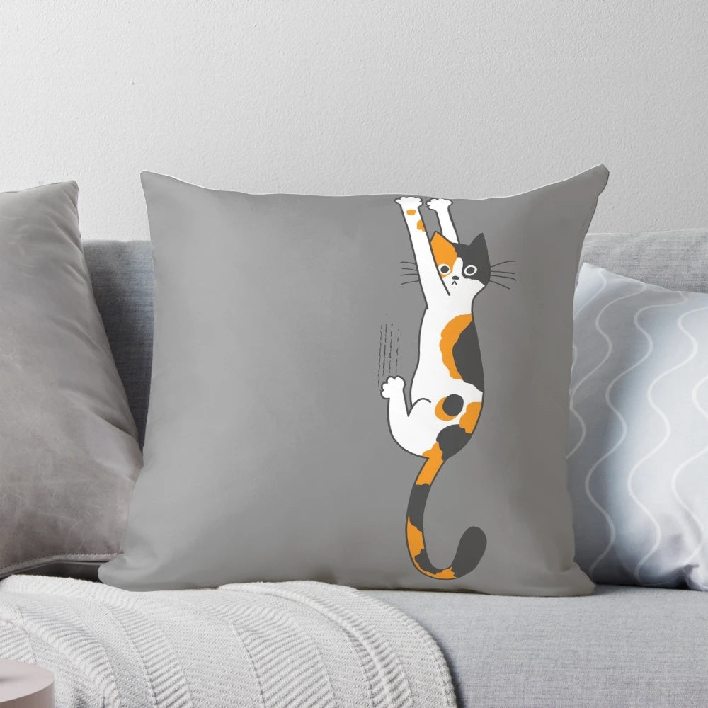 Calico cat humorously clinging to a plush throw pillow