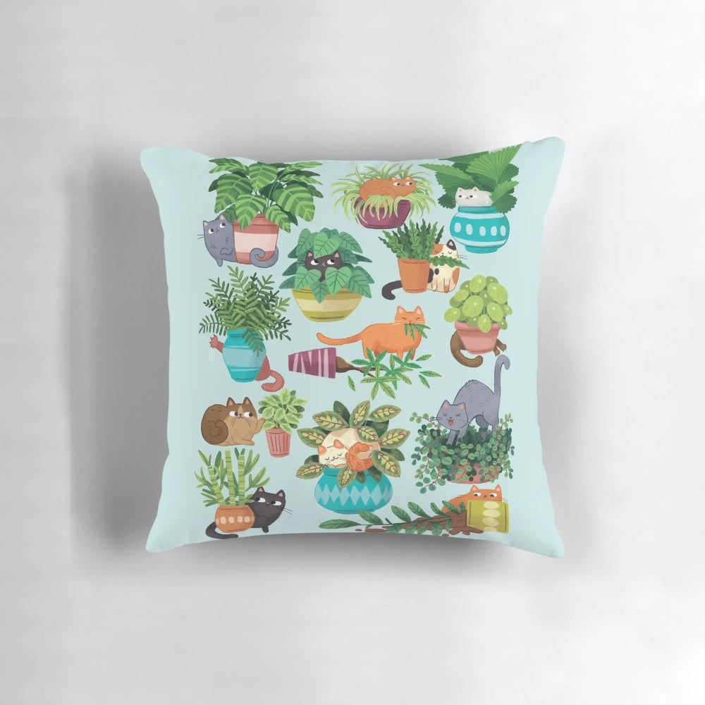 Cute black and tabby cats sitting in a variety of plants on a decorative pillow