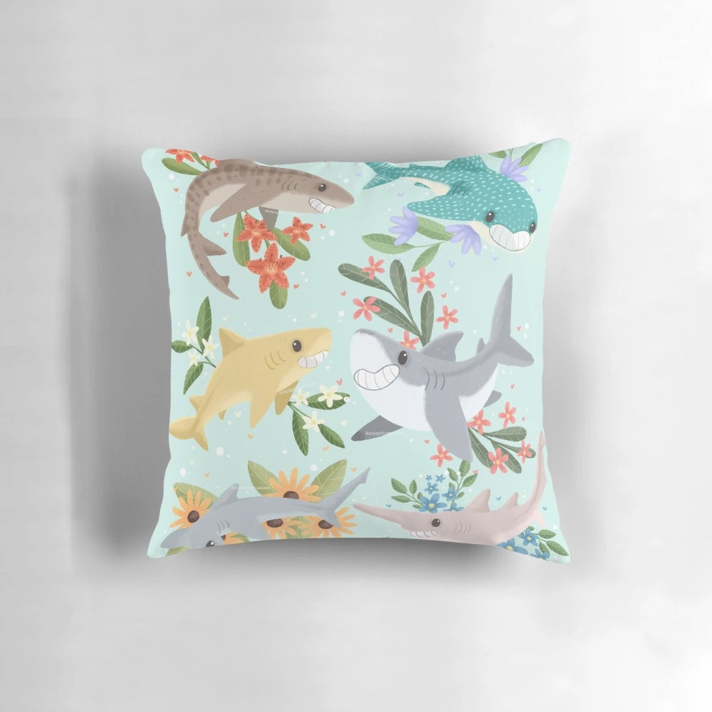 A vibrant, floral-patterned pillow featuring cute, cartoon-style sharks in shades of blue.