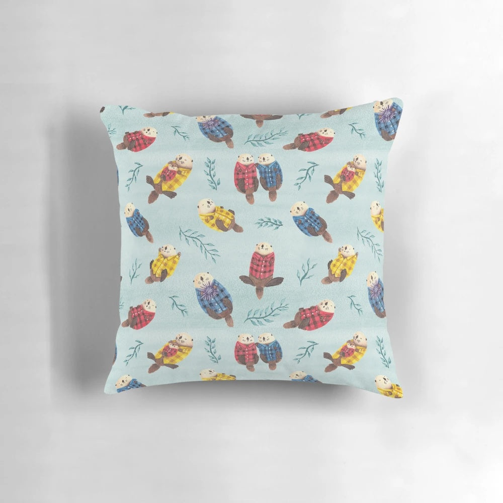 Illustration of two cute, chubby sea otters wearing a plaid, flannel pattern on a decorative pillow.
