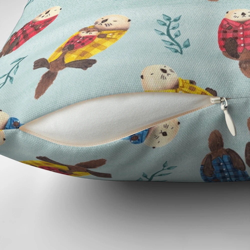 Illustration of two cute, chubby sea otters wearing a plaid, flannel pattern on a decorative pillow.