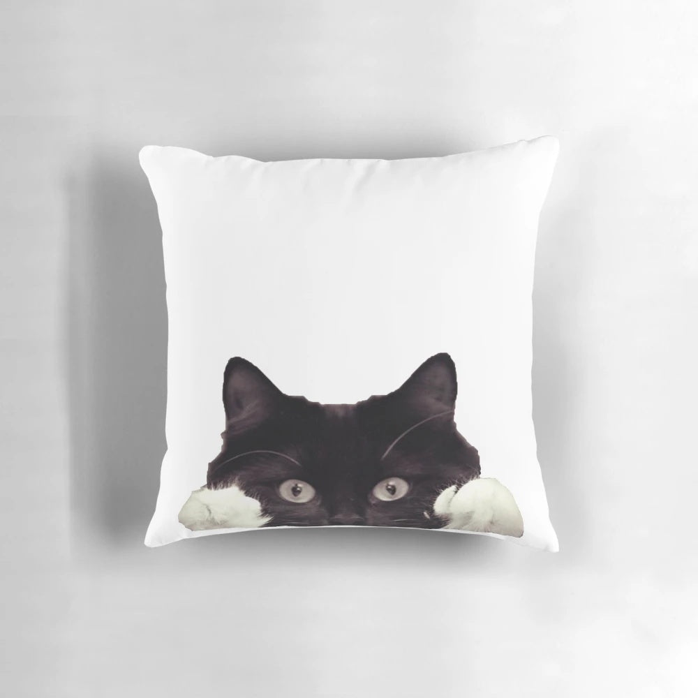 Cute black and white tuxedo cat peeking out from a cozy pillow
