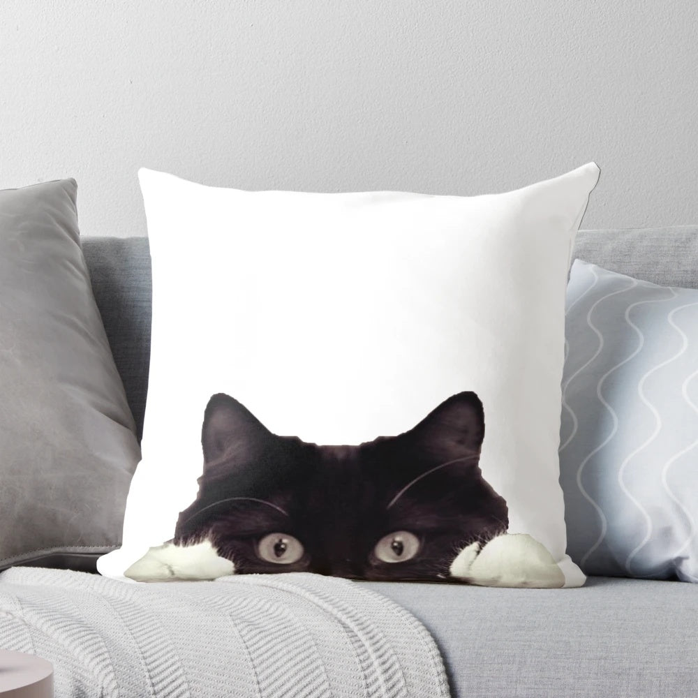 Cute black and white tuxedo cat peeking out from a cozy pillow