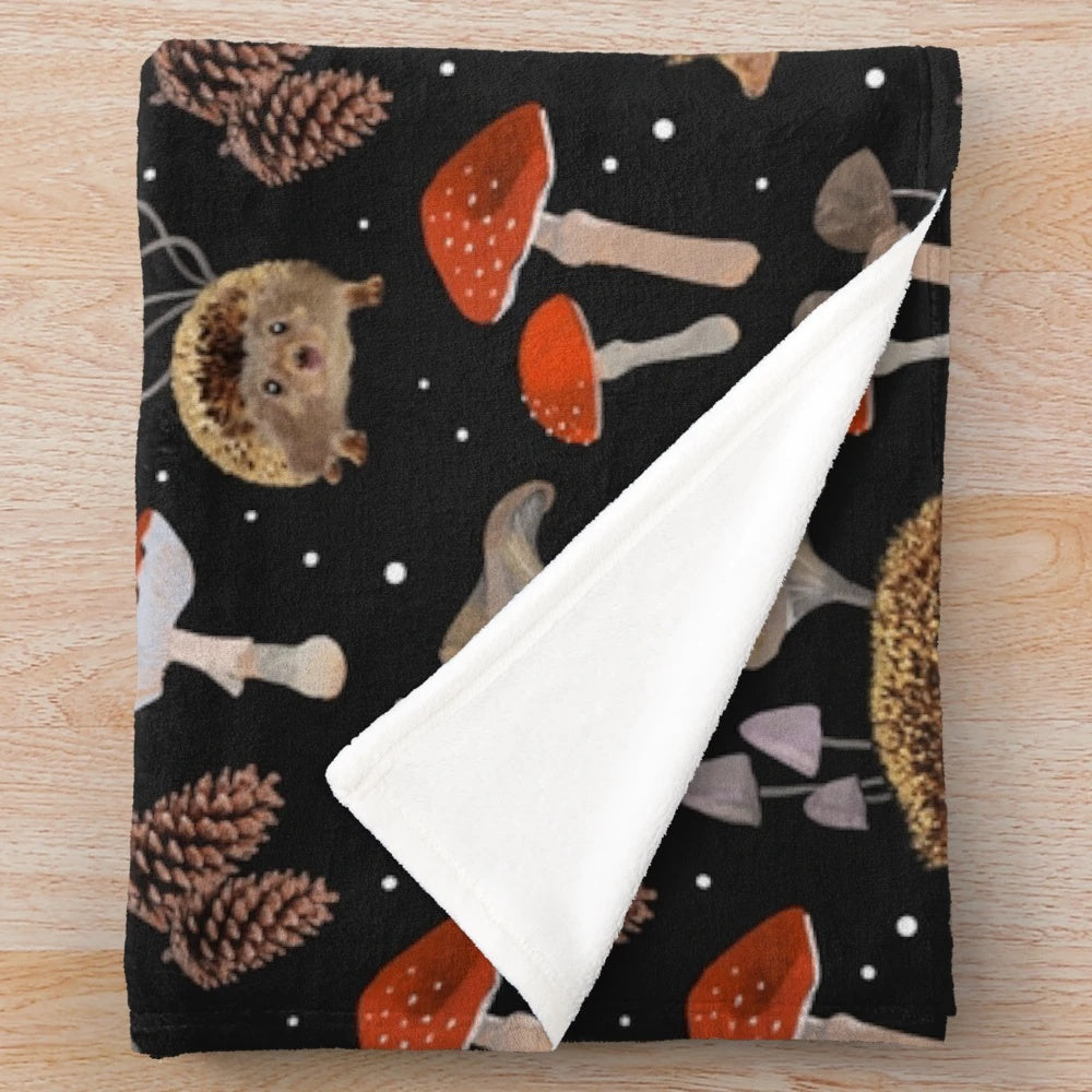 A colorful plush blanket featuring a whimsical design of hedgehogs and mushrooms in an autumn-inspired botanical pattern.