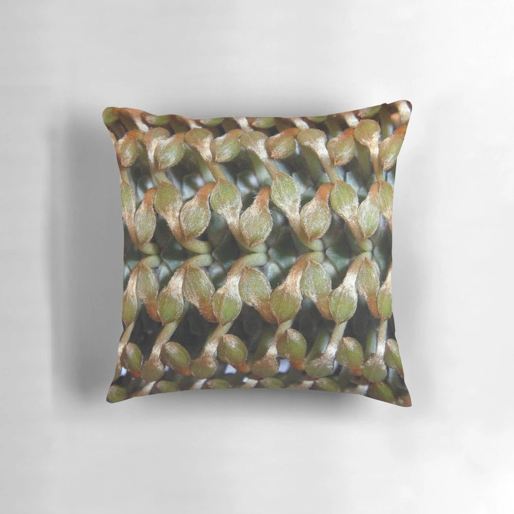 Closeup of a banksia bud on a decorative throw pillow, featuring a botanical pattern in green and orange.