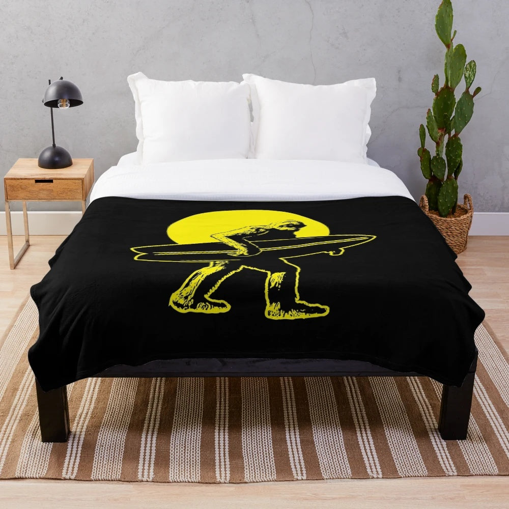 A plush blanket featuring a Bigfoot surfer design, inspired by cryptozoology and alternative culture
