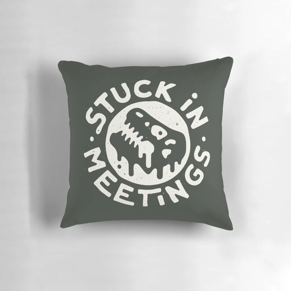 A white pillow with a dinosaur graphic and text reading "Stuck in Meetings
