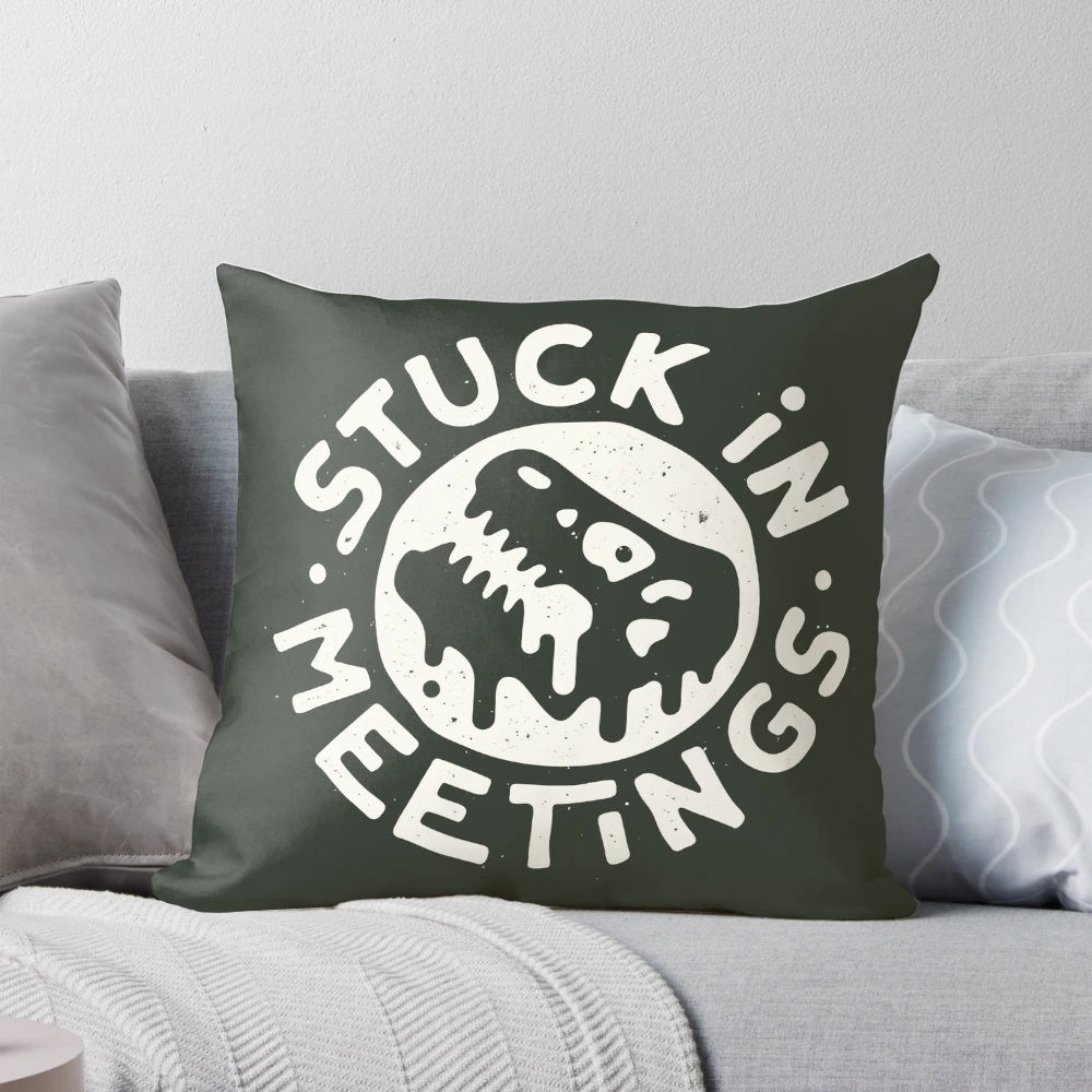 A white pillow with a dinosaur graphic and text reading "Stuck in Meetings