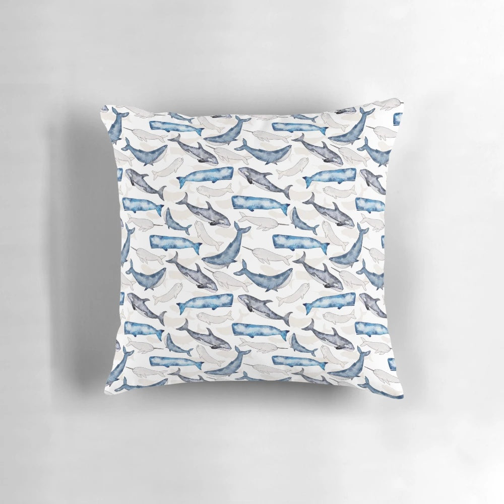 Vibrant watercolor painting of humpback, orca, narwhal, and sperm whales on a blue and turquoise beach-themed throw pillow.