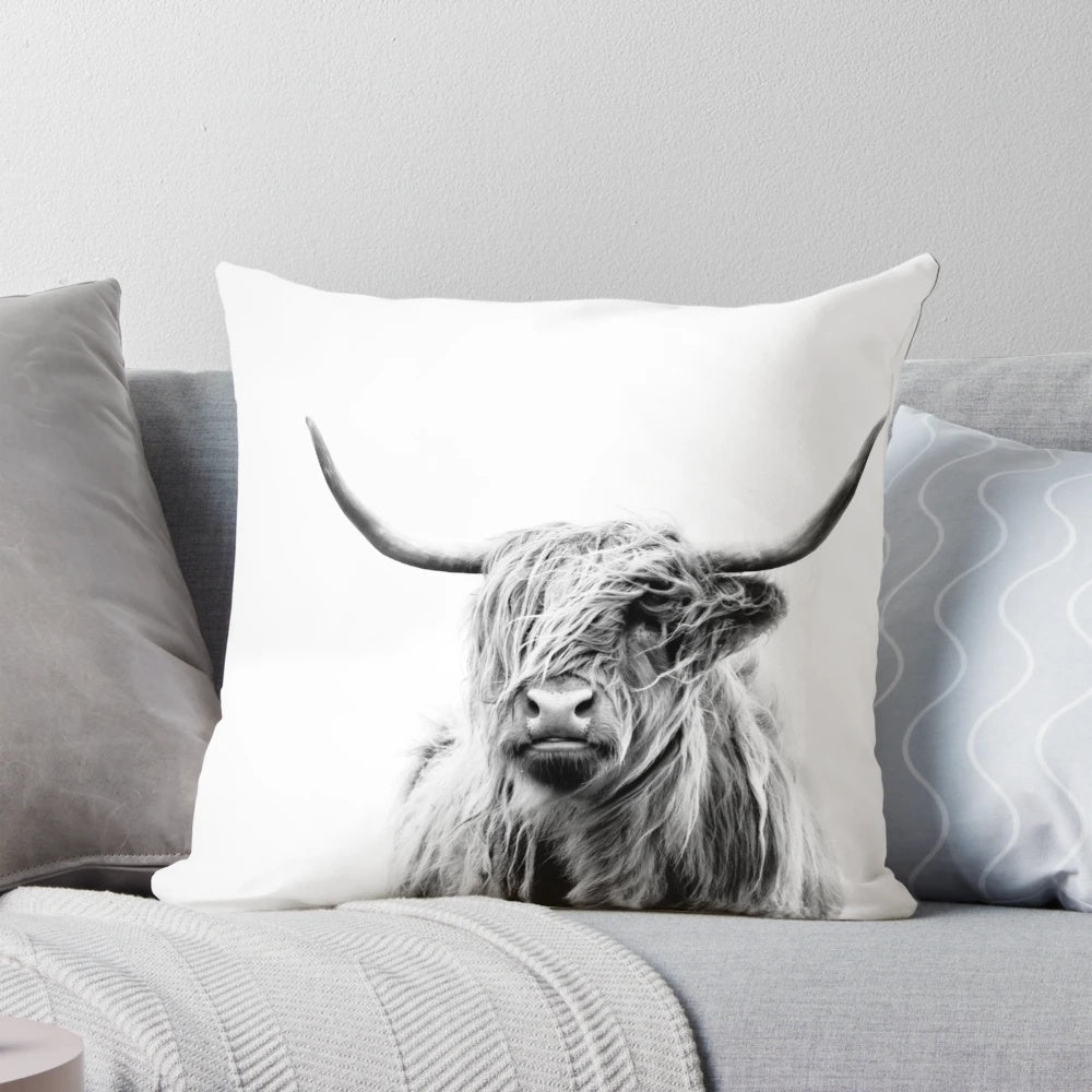 A cozy pillow featuring a portrait of a fluffy, horned highland cow against a warm, rustic backdrop.