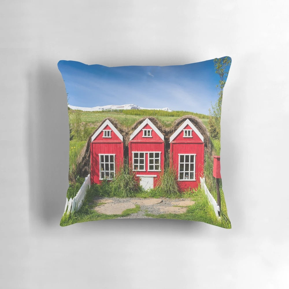 A cozy pillow featuring a whimsical illustration of traditional red elf houses in the Icelandic countryside