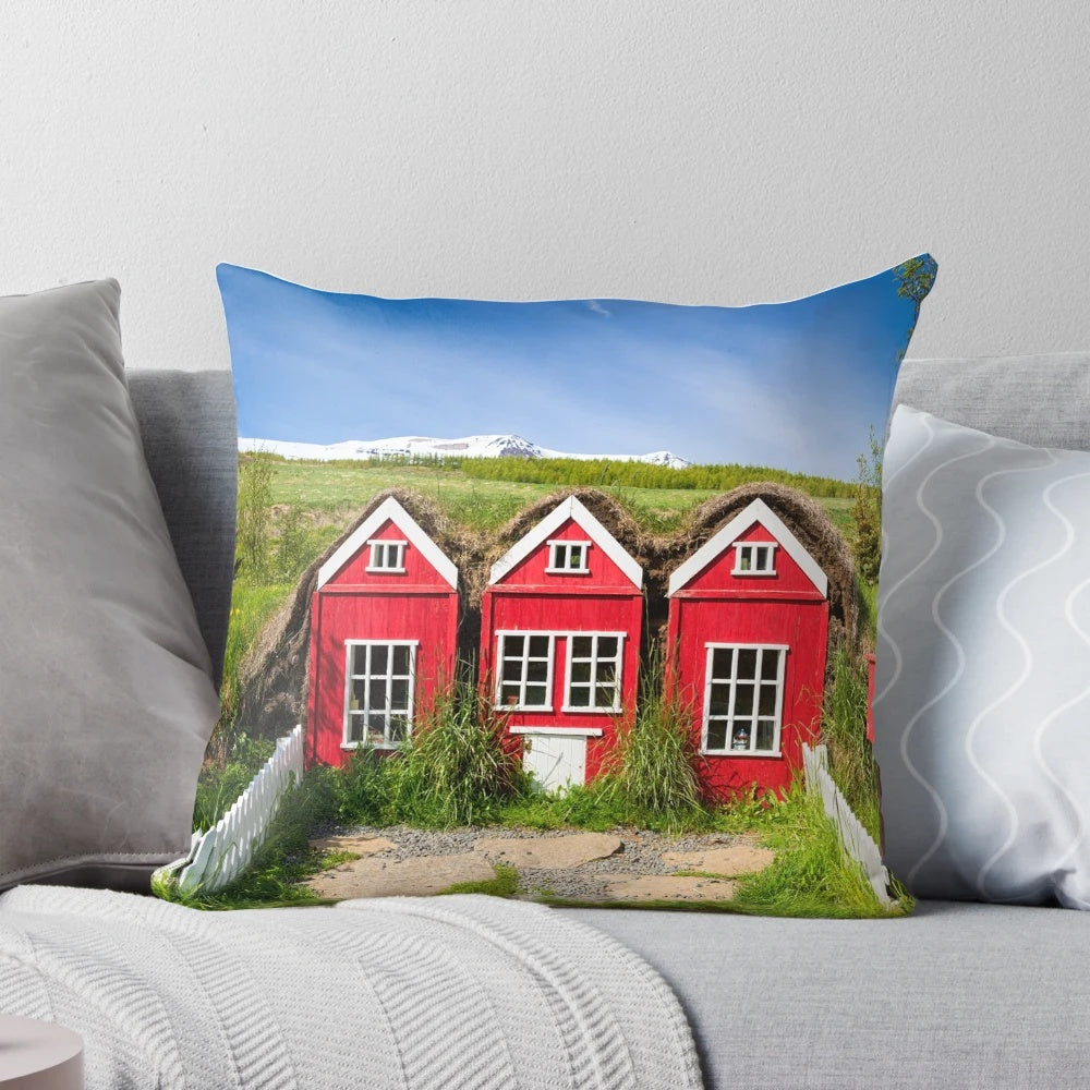 A cozy pillow featuring a whimsical illustration of traditional red elf houses in the Icelandic countryside