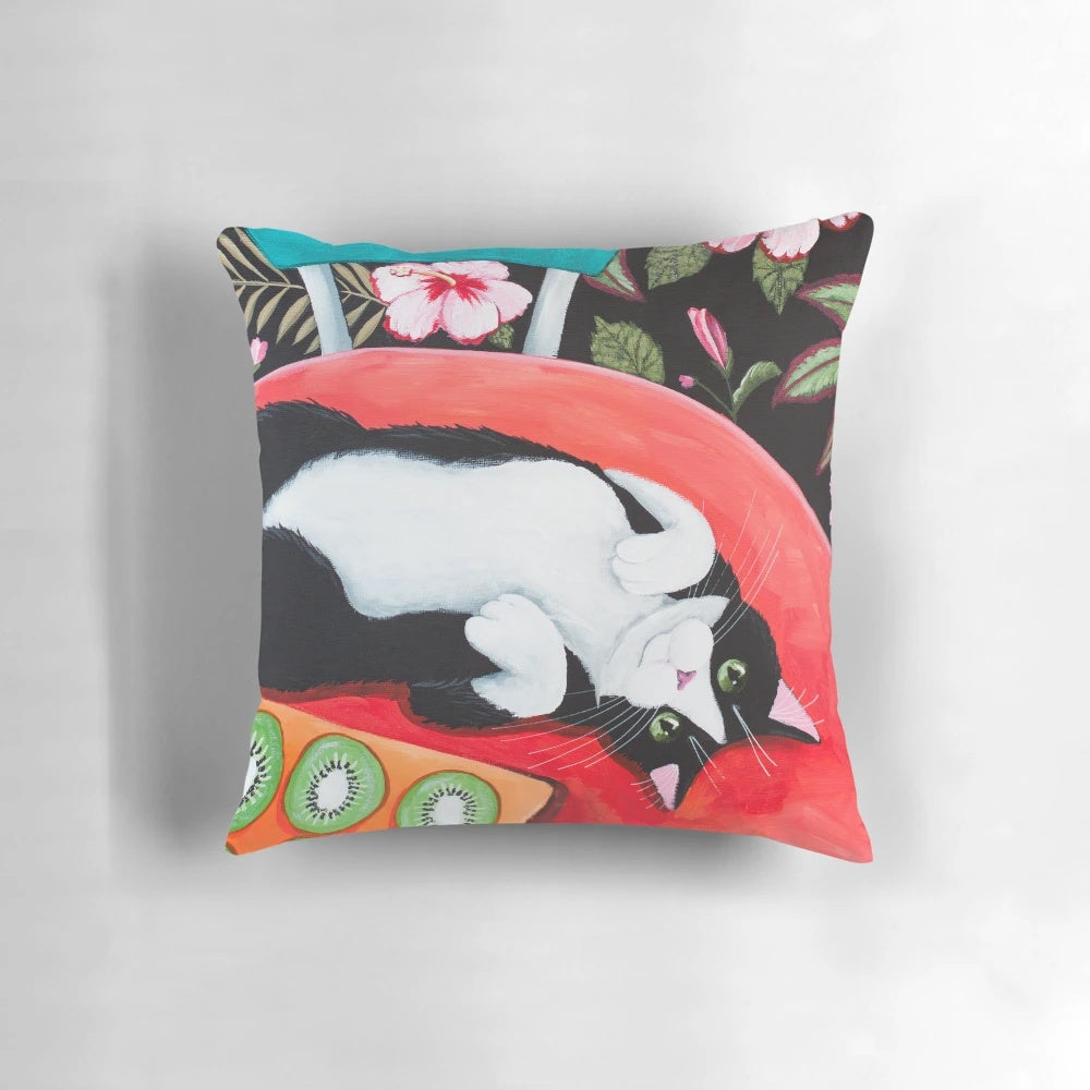 A whimsical throw pillow featuring a tuxedo cat sitting on a kitchen table surrounded by tropical flowers