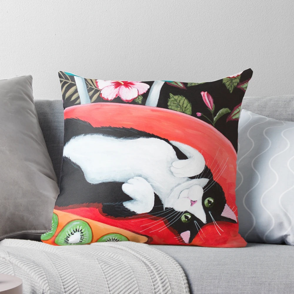 A whimsical throw pillow featuring a tuxedo cat sitting on a kitchen table surrounded by tropical flowers