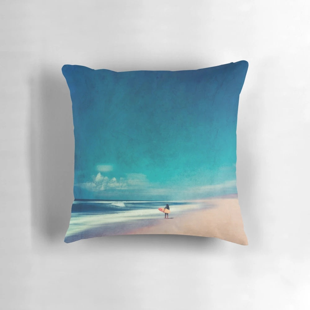 Colorful coastal art pillow depicting ocean waves, a surfer, and a teal and rose landscape for beach house decor.