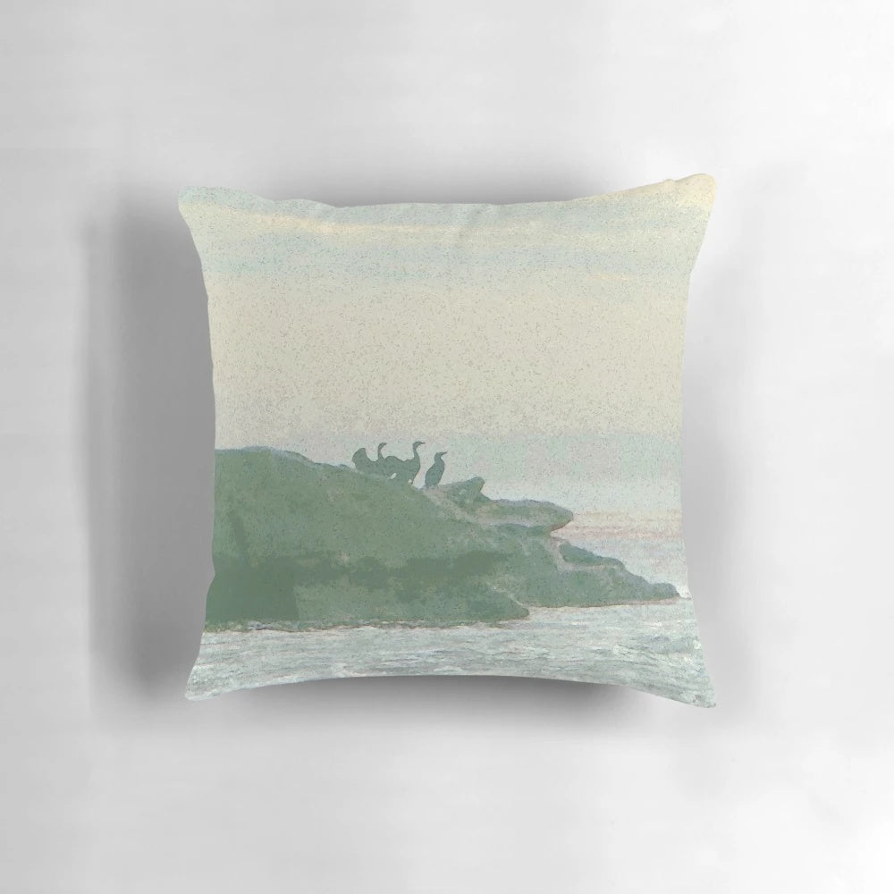 A decorative pillow featuring a design of shorebirds perched on rocky coastal landscape.