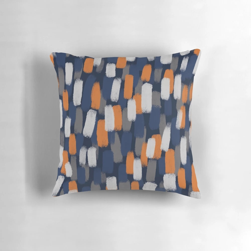 A decorative throw pillow featuring an abstract paint brush design in shades of gray, orange, and blue.
