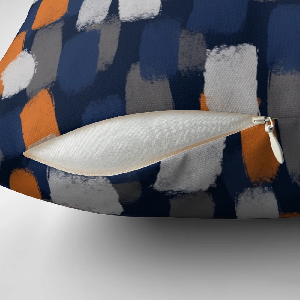 A decorative throw pillow featuring an abstract paint brush design in shades of gray, orange, and blue.