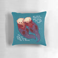 Soft, teal-colored pillow with a hand holding two otters floating on the water