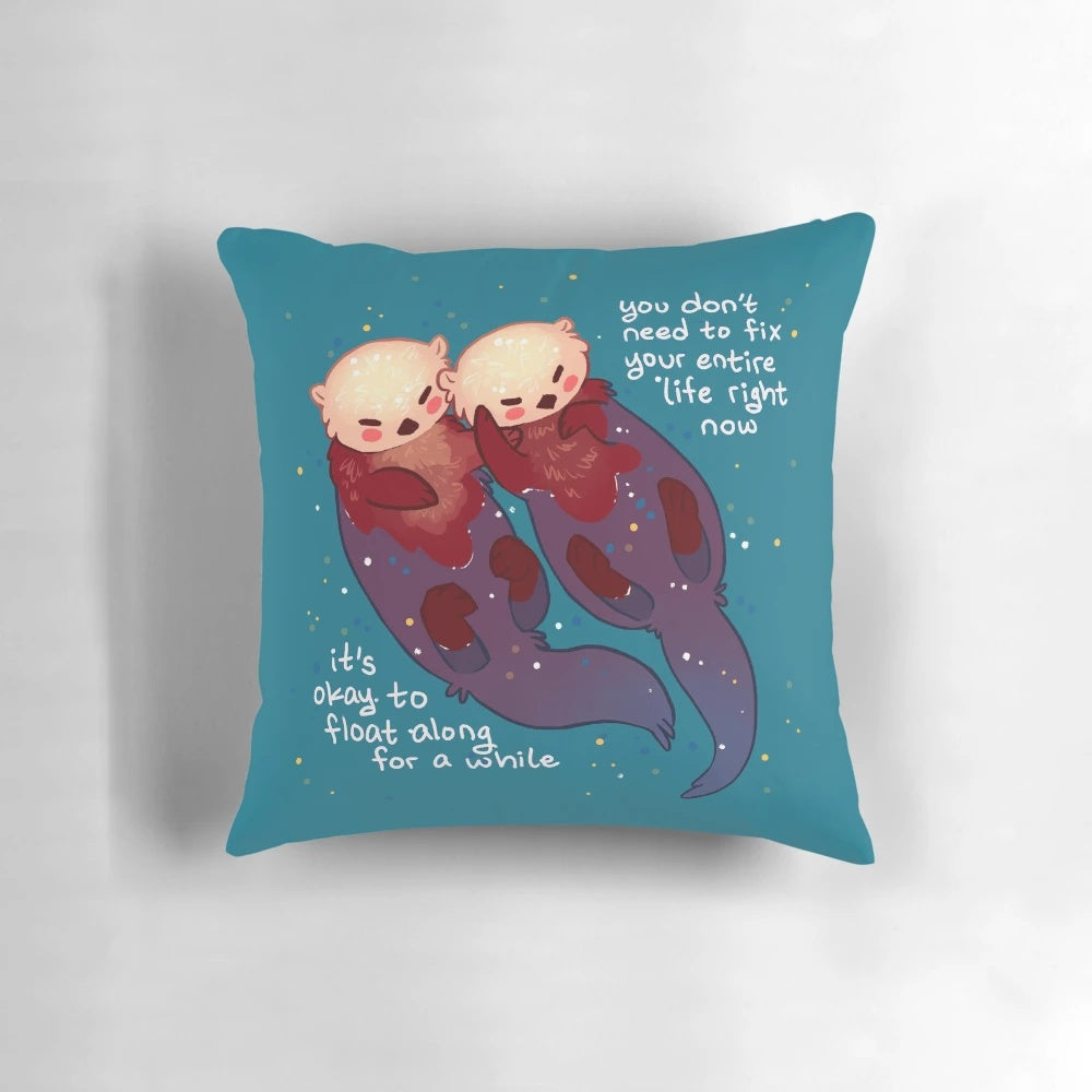 Soft, teal-colored pillow with a hand holding two otters floating on the water