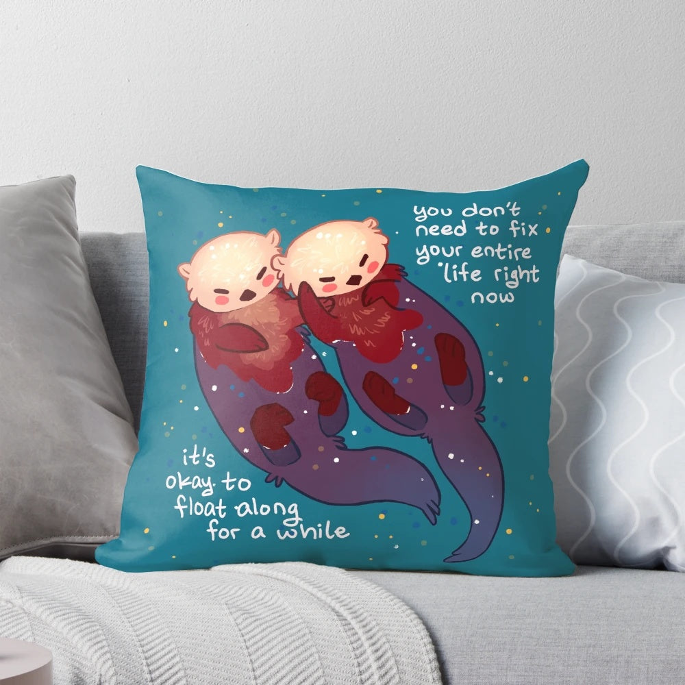 Soft, teal-colored pillow with a hand holding two otters floating on the water