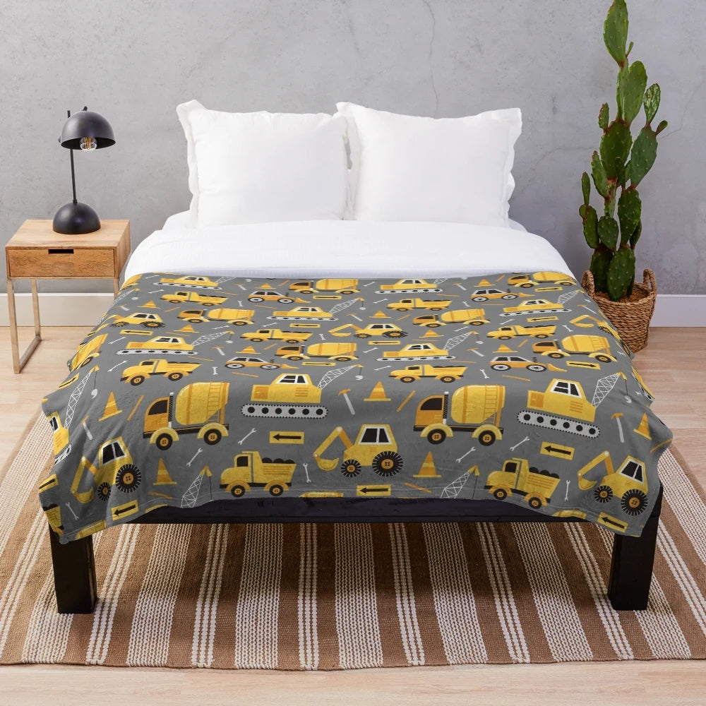 Construction trucks, excavators, and other vehicles printed on a gray plush blanket
