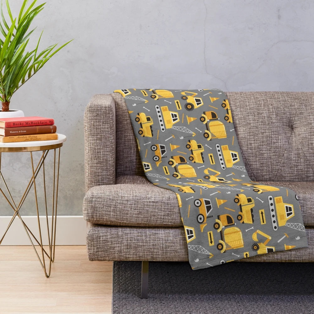 Construction trucks, excavators, and other vehicles printed on a gray plush blanket