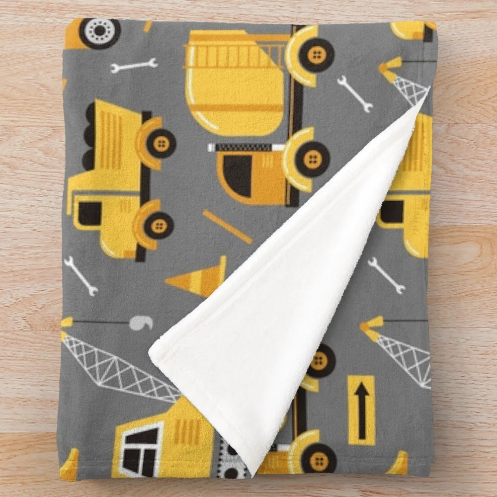 Construction trucks, excavators, and other vehicles printed on a gray plush blanket
