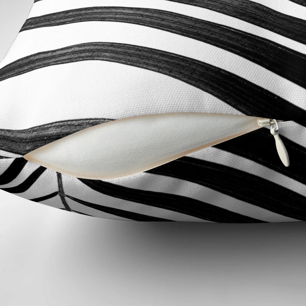 A modern black and white palm leaf design on a decorative throw pillow