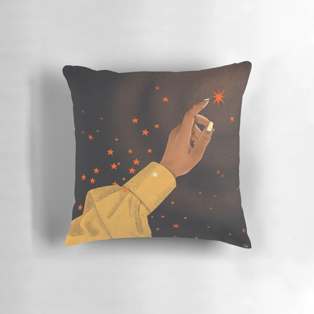 A pillow featuring a hand reaching for the stars against a cosmic, galaxy-inspired background, representing the empowerment of black women.