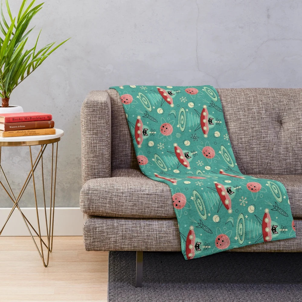 A plush blanket featuring a cat driving a UFO in a retro space-themed design