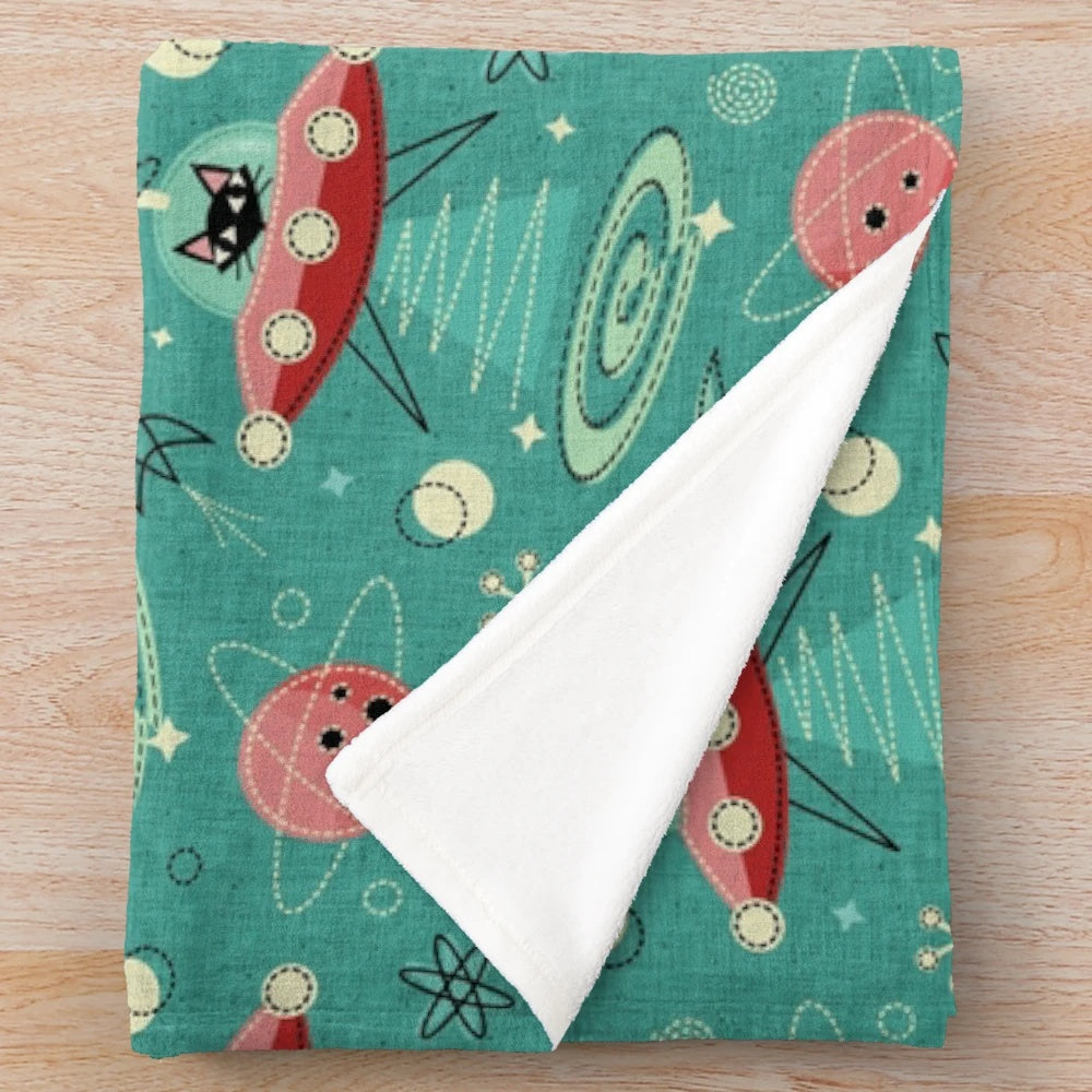 A plush blanket featuring a cat driving a UFO in a retro space-themed design