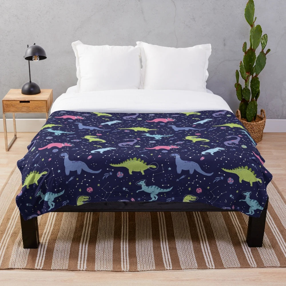 Colorful plush blanket featuring a pattern of space dinosaurs in a purple night sky with stars and constellations