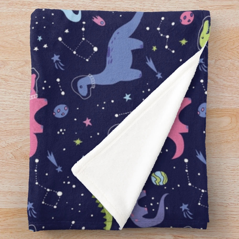 Colorful plush blanket featuring a pattern of space dinosaurs in a purple night sky with stars and constellations
