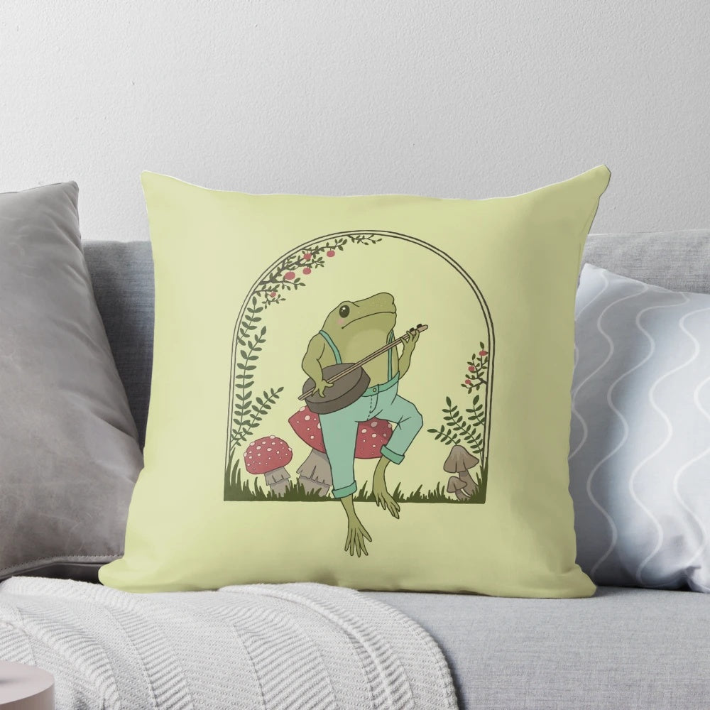 A whimsical cottagecore-style pillow design featuring a frog playing a banjo on a mushroom in a vintage, goblincore-inspired garden setting.