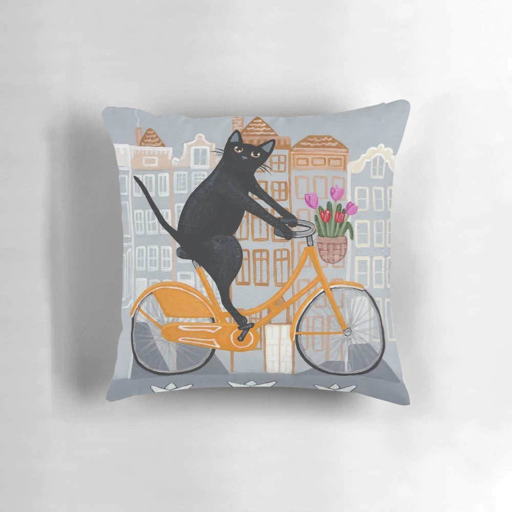 A cozy and whimsical throw pillow featuring a black cat riding an orange bicycle through the streets of Amsterdam.
