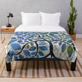A soft, plush blanket featuring a nature-inspired design with blue tones, trees, and whimsical elements.