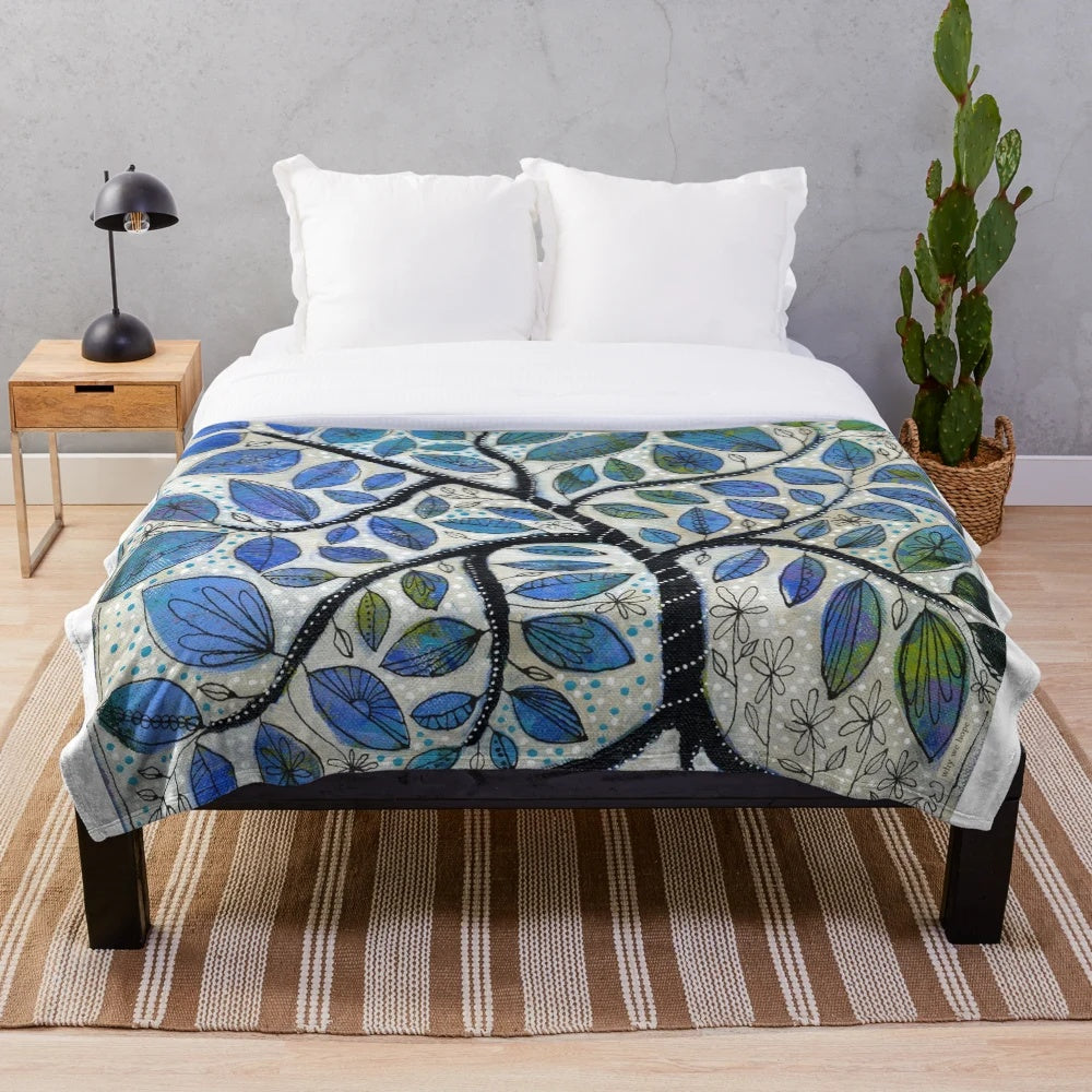A soft, plush blanket featuring a nature-inspired design with blue tones, trees, and whimsical elements.