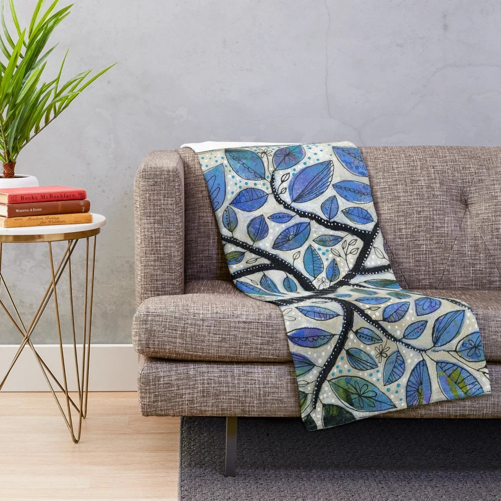 A soft, plush blanket featuring a nature-inspired design with blue tones, trees, and whimsical elements.