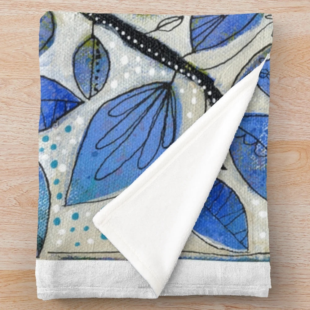 A soft, plush blanket featuring a nature-inspired design with blue tones, trees, and whimsical elements.