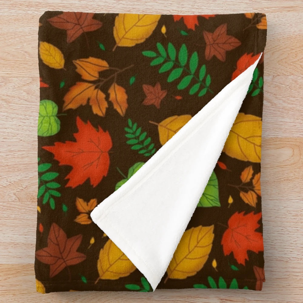 Plush blanket featuring a vibrant autumn leaves pattern in shades of orange, green, and yellow on a brown background