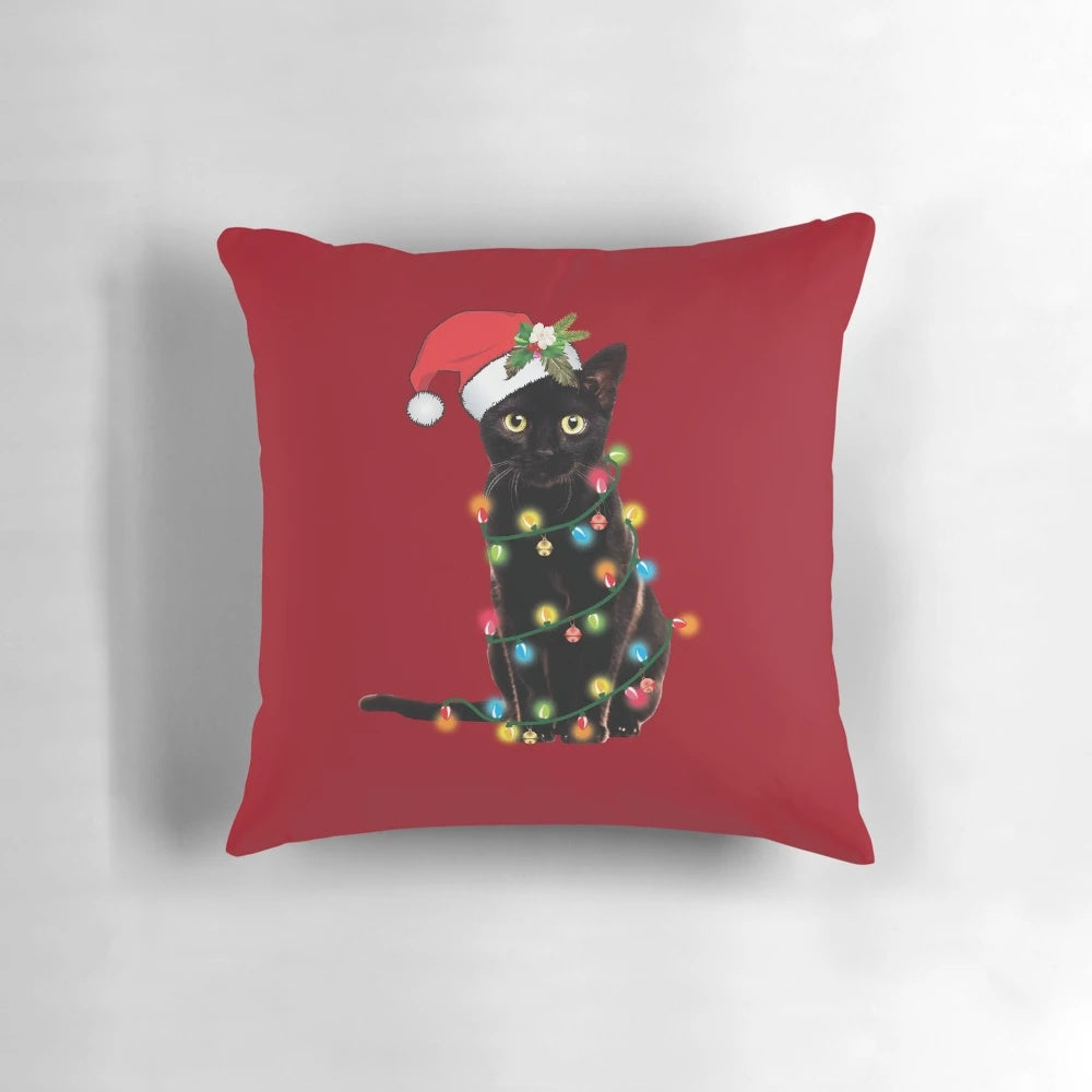 A black cat tangled up in Christmas tree lights, sitting on a festive holiday pillow with a Santa hat.