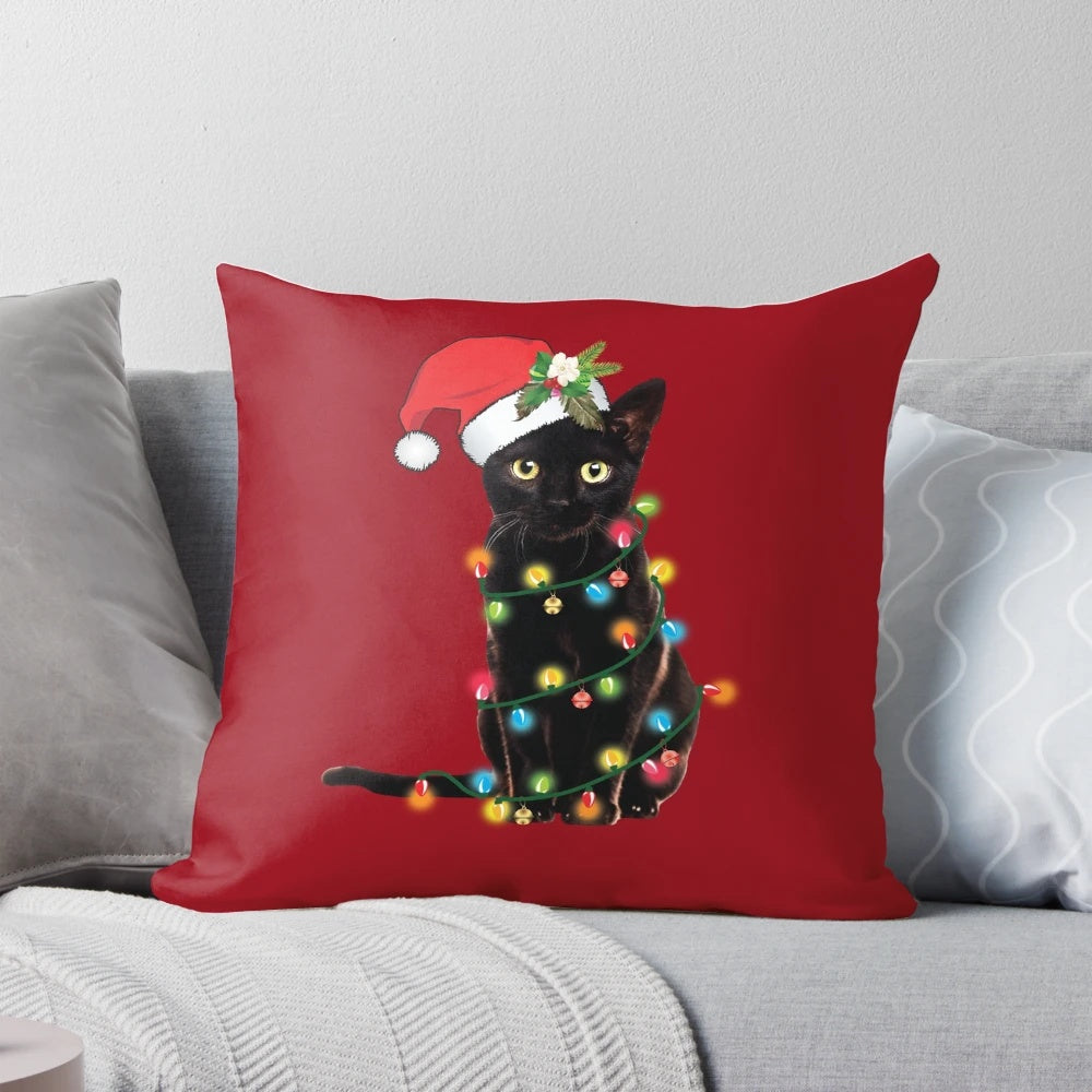 A black cat tangled up in Christmas tree lights, sitting on a festive holiday pillow with a Santa hat.