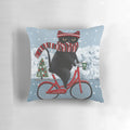 A decorative pillow featuring a black cat riding a bicycle through a winter scene.