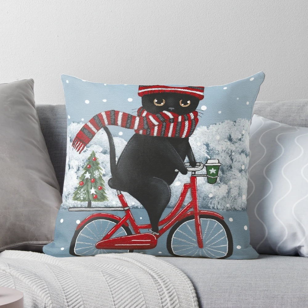 A decorative pillow featuring a black cat riding a bicycle through a winter scene.
