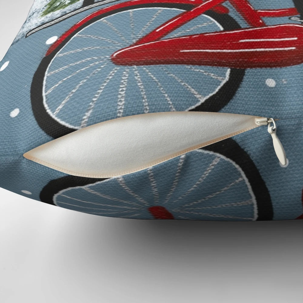 A decorative pillow featuring a black cat riding a bicycle through a winter scene.