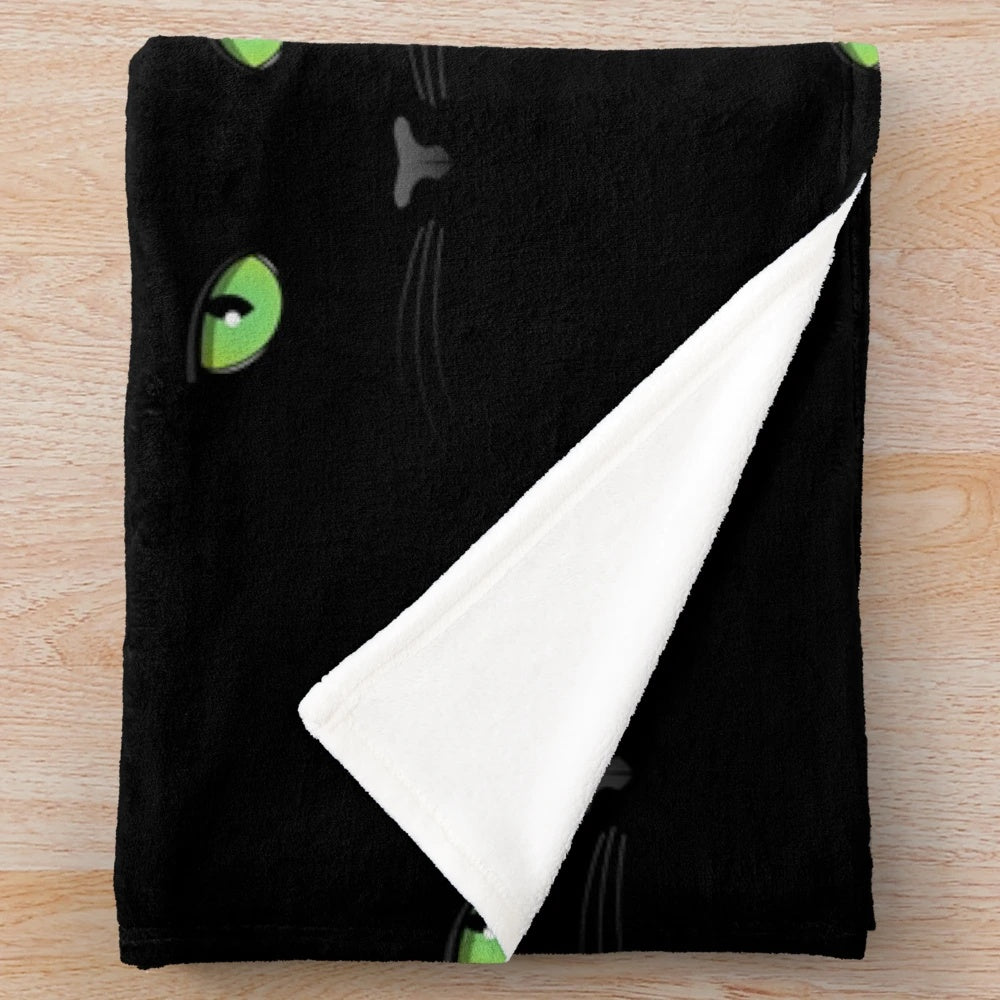 Black cat with green eyes on a plush blanket