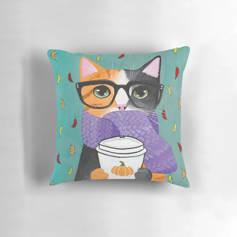 A calico cat wearing glasses and holding a coffee cup, sitting on an autumn-themed pillow