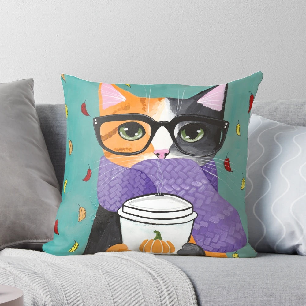 A calico cat wearing glasses and holding a coffee cup, sitting on an autumn-themed pillow